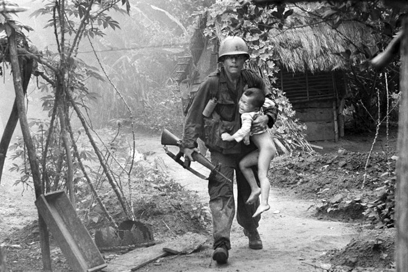 这是越南战争中独具特色的一幕，一位美军士兵抱着越南孩童从烧毁的村庄中走出。这场战争是善良和残忍的矛盾结合体，美军在越南造成了80余万名孤儿，带来无尽的灾难。